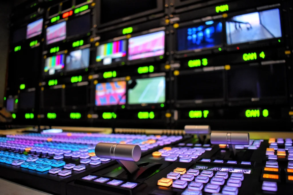 A broadcast table showing buttons, dials and monitor screens